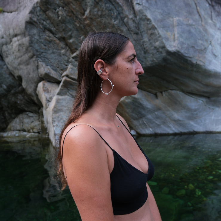 picture of the profile of a woman wearing a square shaped silver ear cuff and a silver hoop, in the background is a river and massive boulders 