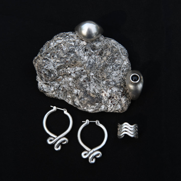 product shoot of sphere rings, big piece of micah, nipple ring with black onyx cabochon, wavy ear cuff , and silver hoops 