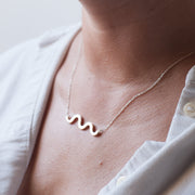 squigle line pentant set on the neck of a woman. she wear a white button down shirt that is open on the neck. 