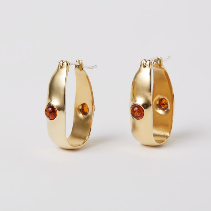 The Oval Hoop is an everyday earring, with a hint of color added by the semiprecious gem. The earrings are made of brass and have a hinged ear wire made of sterling silver. They measure about 1.25" x 0.25". The semi precious gem is Amber and it sits in the front and the back of the earrings.  